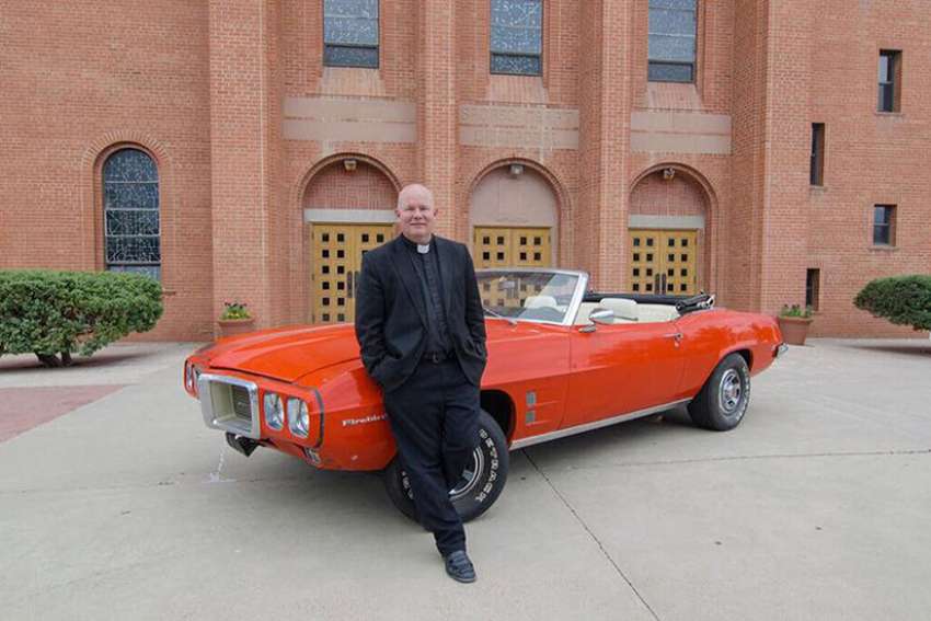 Father Matthew Keller, rector of Sacred Heart Cathedral in Gallup, N.M., poses June 8 with a 1969 Pontiac Firebird Convertible that he refurbished for a raffle in support of vocations for the Diocese of Gallup.