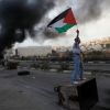 A Palestinian stone-thrower holds a flag as he stands atop a garbage bin during clashes with Israeli security forces near the West Bank city of Ramallah Nov. 18. An Israeli missile ripped through a two-story home in a residential area of Gaza City, killi ng at least 11 civilians, including four young children, in the single deadliest attack of Israel&#039;s offensive against Islamic militants.