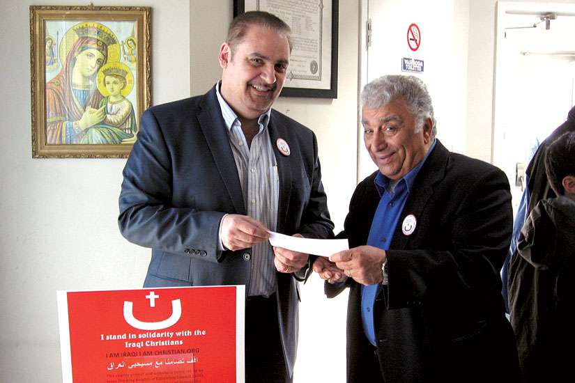 Louay Dawaf, left, receives a donation to aid Iraqi refugees at Jesus the King Melkite Church on April 12.