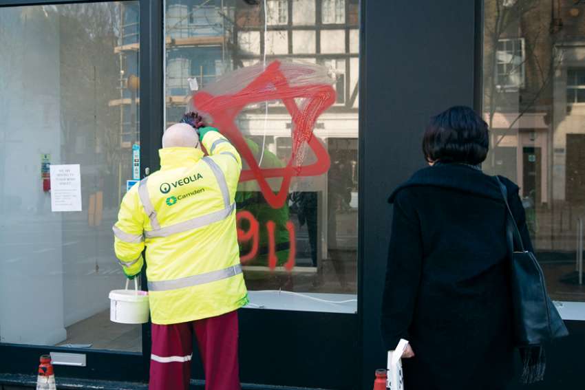 A worker removes anti-Semitic graffiti on a shop window in the Belsize Park neighbourhood of London Dec. 29, 2019.