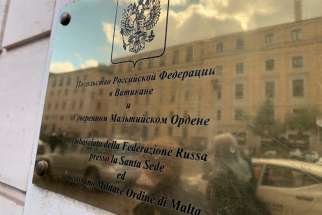 Passersby are reflected in the doorplate of the Russian Embassy to the Holy See on Via della Conciliazione, the main road leading to the Vatican, Feb. 25, 2022. Pope Francis visited the Russian Embassy to the Holy See the same day to express his concern about the war in Ukraine.