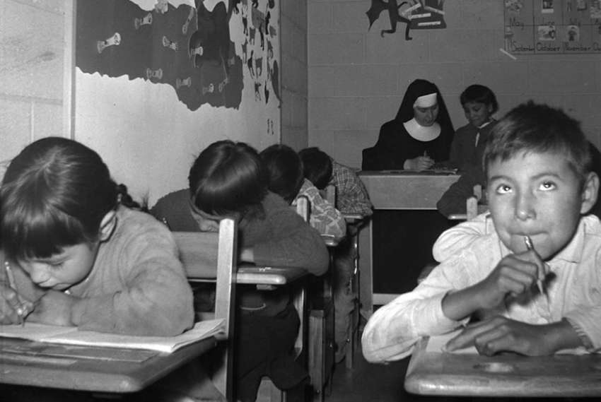 A young boy with other students and a nun in a classroom at the Pukatawagan Residential School, Manitoba, circa 1960.