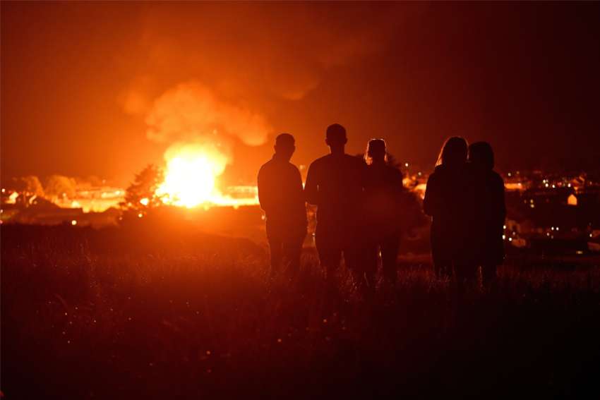 People watch as the completed Craigyhill bonfire burns on the &#039;11th night&#039; to usher in the 12th of July celebrations in Larne, Northern Ireland, July 11, 2022. The Police Service of Northern Ireland said it is investigating a possible crime after an image of Pope Francis was burned in another bonfire in Belfast, Northern Ireland.