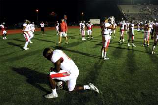 A high school football player prays on the field.