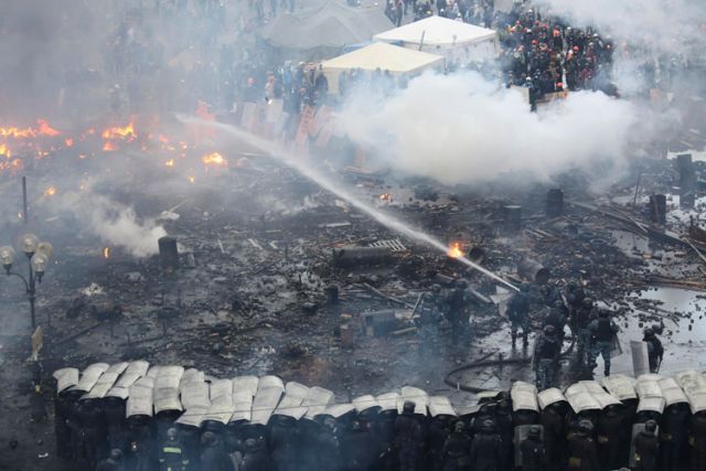 Riot police stand in formation as their colleagues attempt to extinguish a fire during clashes with anti-government protesters in Independence Square in Kiev, Ukraine, Feb. 19. Ukraine&#039;s political crisis escalated sharply, with more than two dozen people killed and scores injured in violent, often fiery battles between demonstrators and police in Kiev.