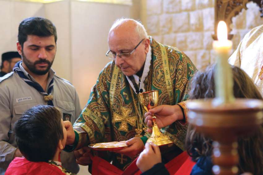 Melkite Archbishop Issam Darwich of Zahle, Lebanon, distributes Communion to Syrian refugee families at the Melkite Catholic archeparchy in Lebanon’s Bekaa Valley in this 2017 file photo. 