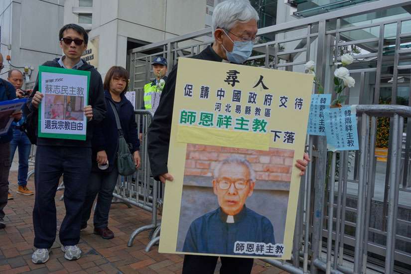 Cardinal Joseph Zen Ze-kiun, retired bishop of Hong Kong, wears a protective mask and holds a picture of Bishop Cosmas Shi Enxiang of Yixian Feb. 14 outside a government building in Hong Kong. Bishop Shi is said to have died under detention.