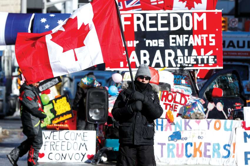 A person waves a Canadian flag in front of banners in support of truckers in Ottawa on Feb. 14, 2022.