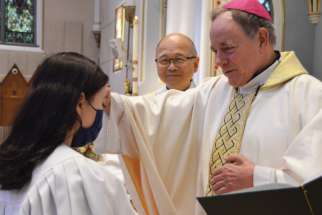 Emma Larson at her baptism April 25. Deacon Richard Chau, who taught her RCIA class, watches while Archbishop J. Michael Miller gives her a blessing.