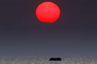 A red sun is seen over a dinghy overcrowded with Syrian refugees drifting in the Aegean sea between Turkey and Greece after its motor broke down off the Greek island of Kos, August 11, 2015.