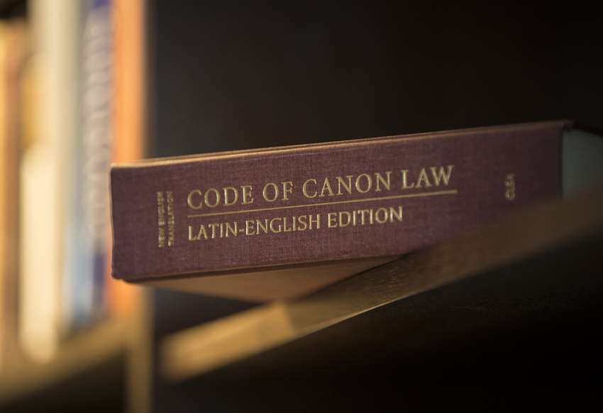 A Latin-English edition of the Code of Canon Law is pictured on a bookshelf.