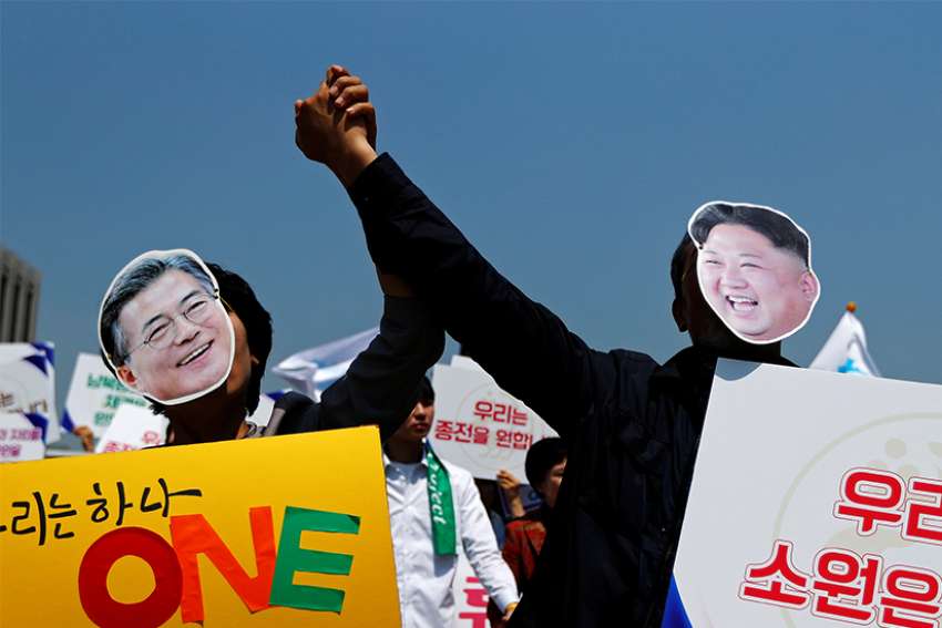 People hold hands and wear masks of South Korean President Moon Jae-in and North Korean leader Kim Jong Un during a unification rally in Seoul, South Korea, April 25. 