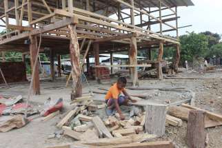  A boy sorts through pieces of wood outside a house being rebuilt in the village of Bigua, Ecuador July 27. Although reconstruction is under way, many families continue to live in tents provided by Catholic Relief Services and Caritas Internationalis. 