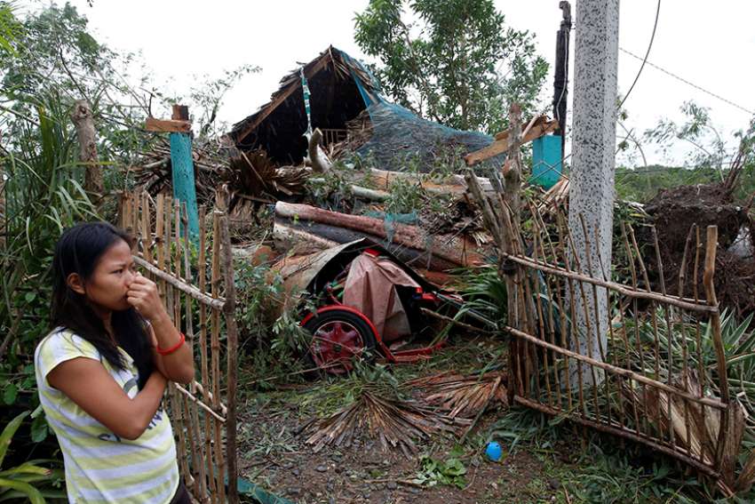 A woman in Bangui, Philippines, stands outside her house damaged by a fallen tree Oct. 20 after Typhoon Haima hit. Typhoon Nock-Ten hit the country Christmas Day.
