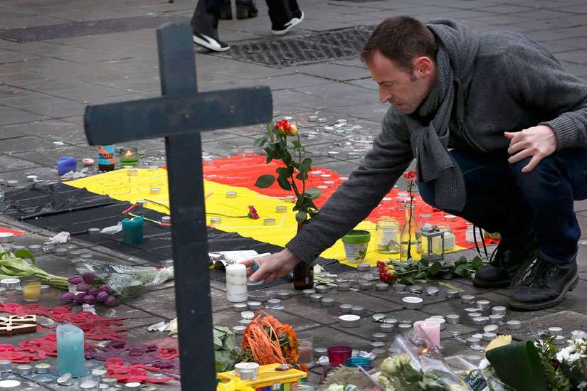 A man places flowers on a street memorial March 23 following bomb attacks in Brussels. Three nearly simultaneous attacks March 22 claimed the lives of dozens and injured more than 200. 