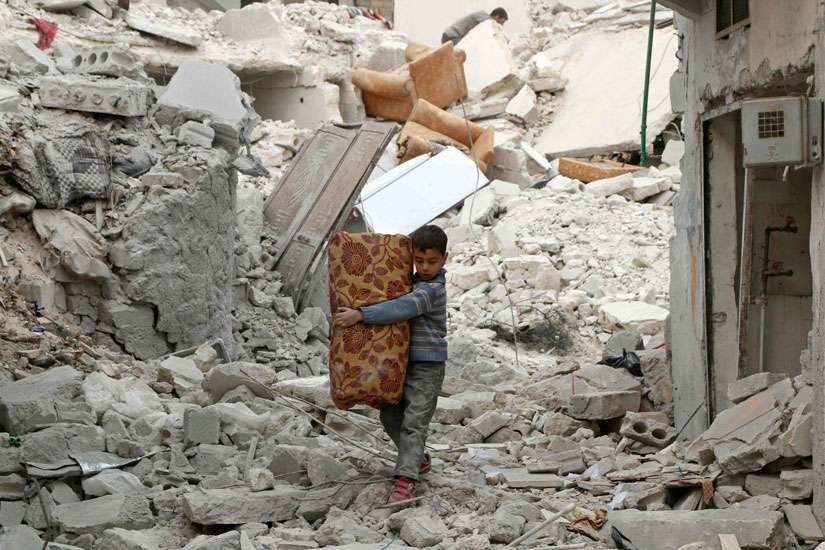 A boy carries belongings Nov. 17 as he walks on the rubble of damaged buildings in Aleppo, Syria. 