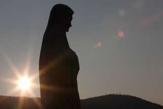 The sun sets behind a statue of Mary on Apparition Hill in Medjugorje, Bosnia-Herzegovina. 