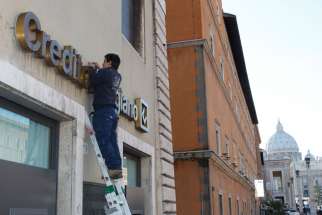 A man repairs a bank sign on Via della Conciliazione, the road leading to the Vatican Jan. 29. 