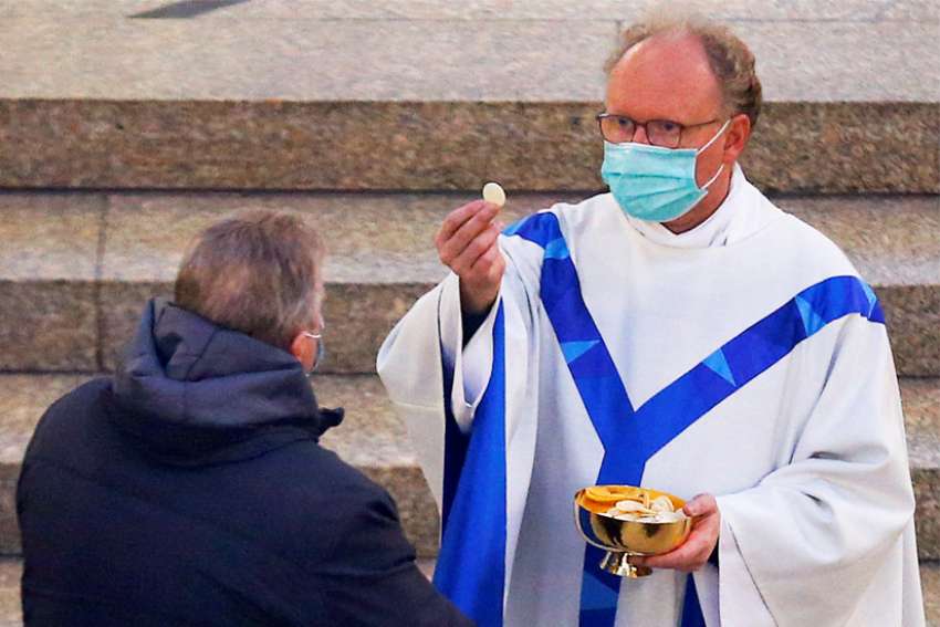 A priest wearing a protective face mask gives holy Communion to a man May 1, 2020, in a Catholic church in Kevelaer, Germany, during the first public Mass in the city since churches were closed because of the coronavirus pandemic.
