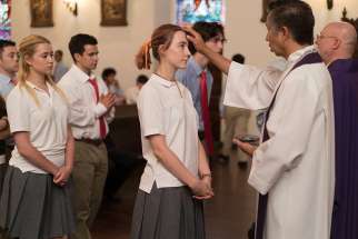 Fr. Paul Keller vested in purple applies ash on a young man&#039;s forehead during the Ash Wednesday scene in Lady Bird. 