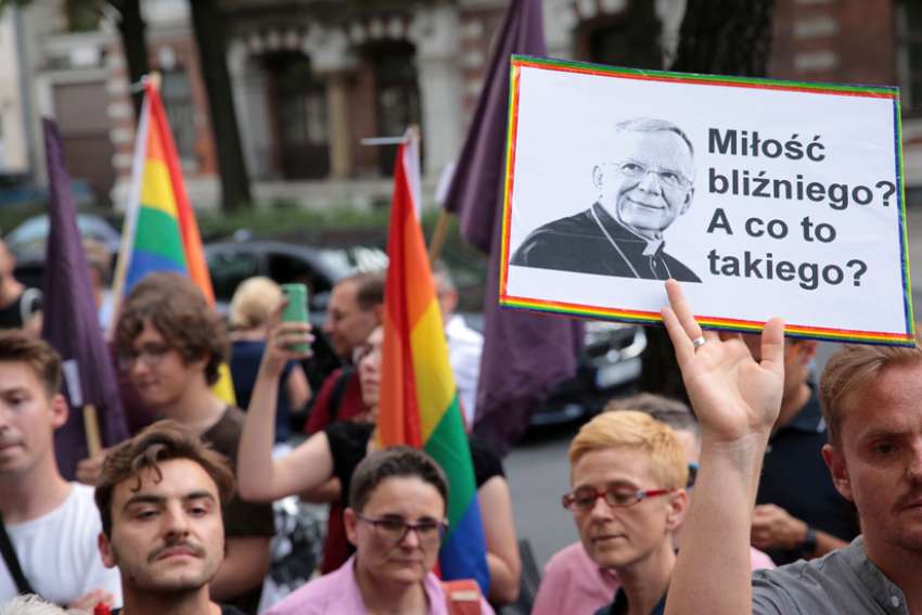 People in Warsaw, Poland, gather outside the apostolic nunciature Aug. 7, 2019, to demand the resignation of Archbishop Marek Jedraszewski of Krakow. The protesters were upset that the archbishop had likened the LGBTQ community and the rainbow flag to a &quot;communist plague.&quot; The placard reads &quot;Love of a neighbor? What&#039;s this?&quot;