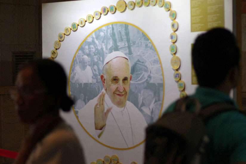 Filipinos walk past a picture of Pope Francis Nov. 20 at a museum dedicated to the pope inside a Manila cathedral where he is scheduled to celebrate Mass during his Jan. 15-19 trip to the Philippines. Philippine church officials say pope&#039;s visit will bri ng healing to the country, which was devastated by a 2013 typhoon.