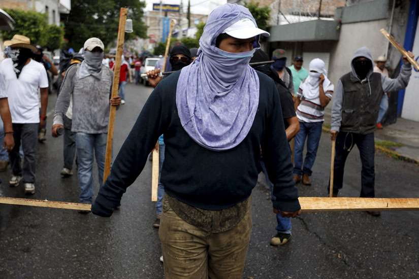 Demonstrators hold batons as they take part in a Sept. 27 march to mark the first anniversary of the disappearance of 43 students from a teachers college in the southern Mexican state of Guerrero. The Mexican bishops&#039; conference and the Vatican have confirmed Pope Francis will visit Mexico in 2016.