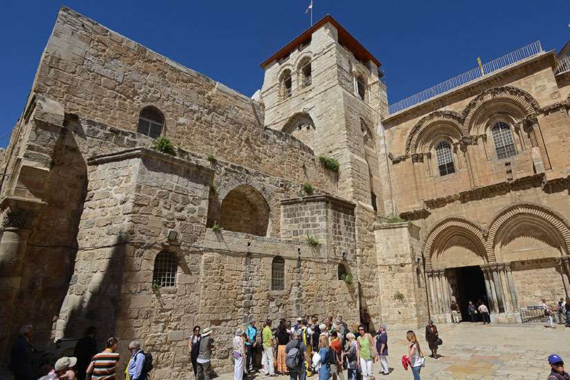 Pilgrims stand outside the Church of the Holy Sepulchre in Jerusalem’s Old City while below a woman prays inside the church. Hundreds of thousands of pilgrims are drawn to the site year round, but never so much as during Holy Week. Biblical scholar Murray Watson said pilgrims become conscious of walking on holy ground and “being at the literal heart of the Christian Gospel.”