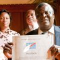 United Methodist Bishop Ntambo Nkulu Ntanda displays one volume of the million-plus name petition to the United Nations demanding meaningful peacekeeping and serious consequences for the Rwandan government for supporting militias in the eastern Democratic Republic of Congo. Behind him are Mme. Emma Zanao Selenani and Prof. Raymond Mande Mutombo.