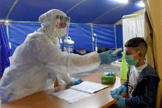 A nurse wears a protective suit while taking the temperature of a Palestinian boy in a special tent for pediatric and maternity COVID-19 patients at St. Joseph&#039;s Hospital in East Jerusalem April 16, 2020.