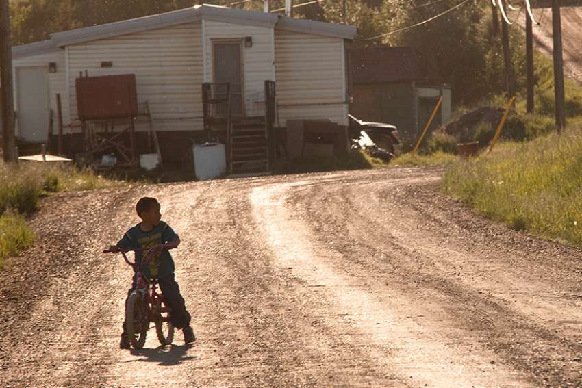 A young boy rides his bike around his neighbourhood on an Indigenous reserve. 