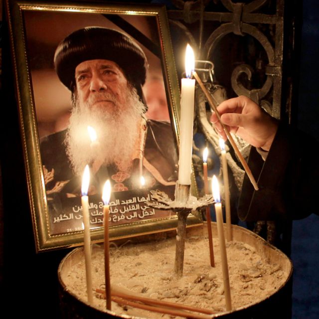 In Jerusalem&#039;s Church of the Holy Sepulcher March 18, a priest lights a candle in front of a picture of Coptic Orthodox Pope Shenouda III of Alexandria, Egypt. Pope Shenouda, who served as patriarch of the Coptic Orthodox Church for 41 years, died March 17 at the age of 88.