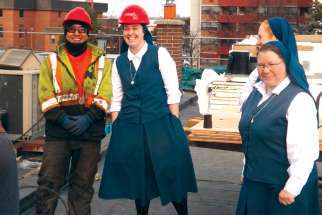 Sr. Carly Paula Arcella joins the hard-hatted crew on the roof of Pauline Books &amp; Media Centre while local superior Sr. Catherine Bennett, right, and Sr. Amanda Marie Detry, background, look on.
