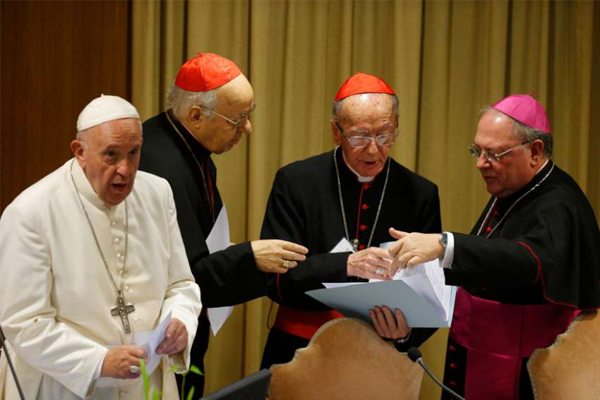 Pope Francis is pictured as Cardinal Lorenzo Baldisseri, secretary-general of the Synod of Bishops, Brazilian Cardinal Claudio Hummes, relator general of the synod, and Bishop Fabio Fabene, undersecretary of the Synod of Bishops, talk at the start of the final session of the Synod of Bishops for the Amazon at the Vatican Oct. 26, 2019.