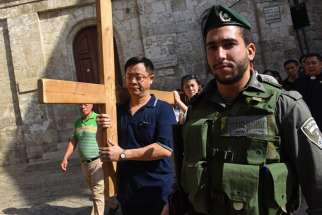 An Israeli border police officer stands near Catholic tourists from Indonesia as they carry a cross Oct. 18 on the Via Dolorosa in Jerusalem&#039;s Old City, near a site where several recent stabbings have taken place.
