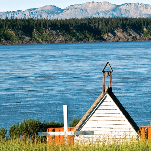 The Mackenzie River slips by the old Anglican church in Tulita with the Mackenzie Mountains in the background. The church built in 1880 is now an historic site and a testament to the 200-year Christian history of the Sahtu region in the Northwest Territories.