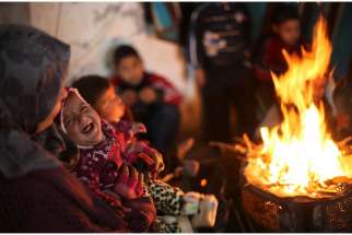 A baby cries as members of a Palestinian family warm themselves by a fire Feb. 20 at the remains of their house that witnesses said was destroyed by Israeli shelling during a 50-day war last summer near Gaza City. Six months after the end of the most rec ent war in Gaza, one aid official said there is still a &quot;grave humanitarian crisis.&quot; 