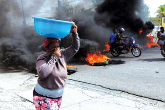 A woman covers her nose while walking past a burning road block in Port-au-Prince, Haiti.