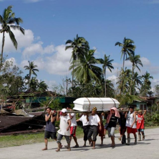 Residents carry the coffin of a victim of Typhoon Bopha Dec. 6 past a house destroyed by the typhoon in New Bataan, Philippines. Catholic Relief Services and Caritas Philippines planned to begin distributing basic necessities to 1,250 families as soon as possible.