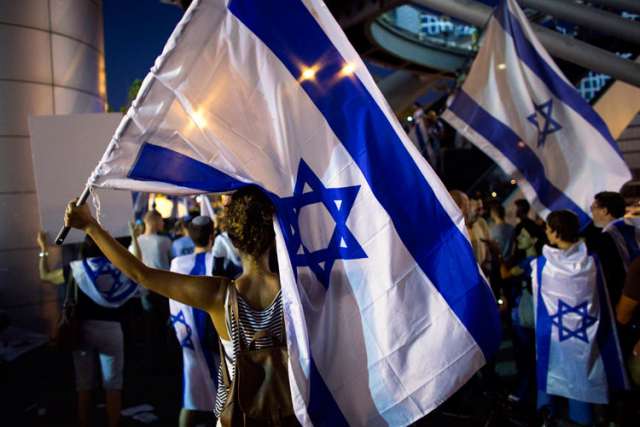 Activists hold flags in Tel Aviv, Israel, July 29 to show support for Israel&#039;s offensive in the Gaza Strip. Tour operators interview by Catholic News Service say the ongoing violence in Middle East has not affected pilgrimages to the Holy Land.