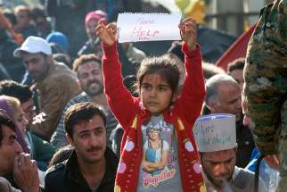 An Iranian girl raises a sheet of paper with &#039;Please HELP Me&#039; on it Nov. 24 as a group of people wait for permission to cross the border from Greece into Macedonia. Macedonia began granting entry only to refugees from Syria, Iraq and Afghanistan.